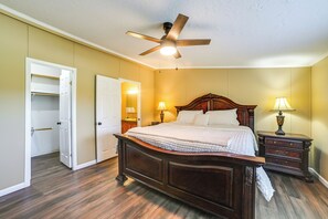Une chambre à coucher avec un lit en bois, deux tables de chevet avec des lampes, un ventilateur de plafond et une porte donnant sur un placard.