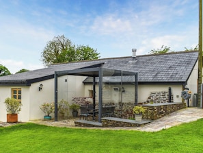 Ein Haus mit überdachter Terrasse, Steinmauer und kleinem Garten.