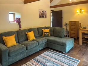 A living room with a sectional sofa, a patterned rug, and a wooden dining table. - 2 bedroom accommodation in Holsworthy (Holsworthy)