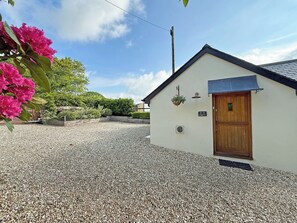 A building with a gravel driveway, a wooden door, and a hanging flower basket. - 2 bedroom accommodation in Holsworthy (Holsworthy)