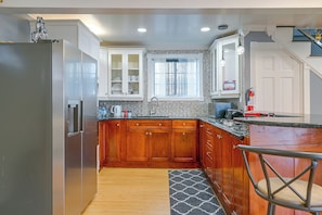 A kitchen with wooden cabinets, a stainless steel refrigerator, a window with curtains, and a fire extinguisher. - Updated Schenectady Home: 1 Mi to Downtown! (Schenectady)