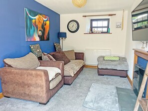 A living room with a blue wall, a painting of a horse, a clock, a window, and a fireplace. - Another Dawn - UK52026 (Wigton)