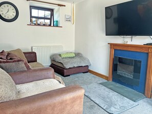 A living room with a brown leather sofa, a small ottoman, a fireplace, a television, and a wall clock. - Another Dawn - UK52026 (Wigton)