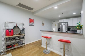 A modern kitchen with a built-in stove, a refrigerator, and a coffee machine. There are two red bar stools and a metal shelf with kitchen utensils. - Viva La Dolce Vita in the Heart of Little Italy! (San Diego)