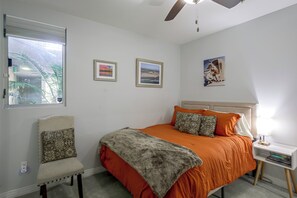 Ein Schlafzimmer mit einem Bett, einem Sessel, einem Nachttisch und einem Fenster.