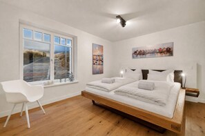 Une chambre avec un grand lit, une chaise blanche et une fenêtre donnant sur une plage.