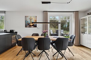 A modern dining area with a wooden table, black chairs, and a painting of an anchor on the wall. - Senhüs - Stylish cottage for 6 people with a sauna, garden, and free E (Hörnum (Sylt))