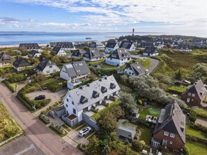 An aerial view of a coastal residential area with houses, a lighthouse, and a pier in the background. - Senhüs - Stylish cottage for 6 people with a sauna, garden, and free E (Hörnum (Sylt))