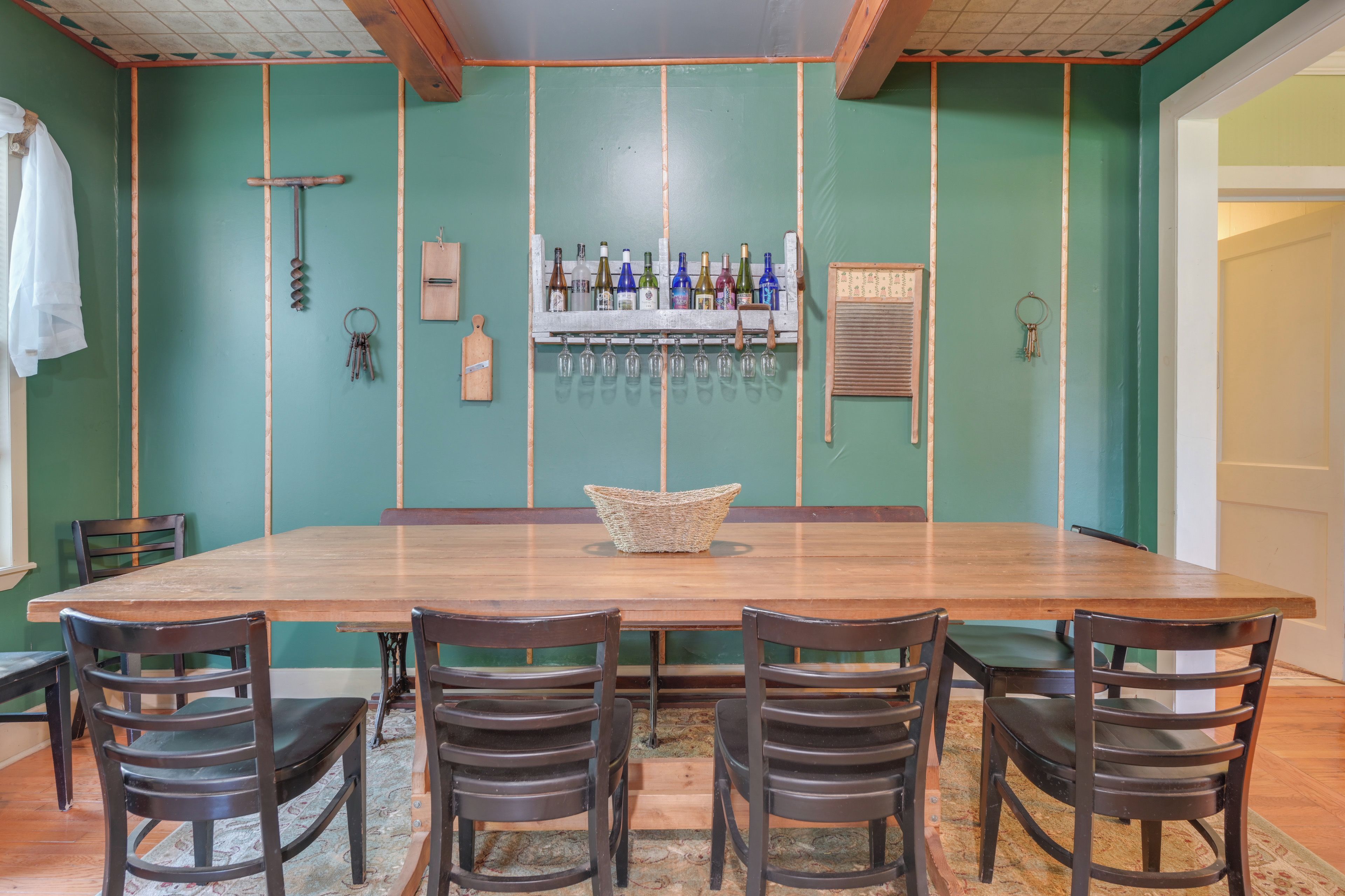 Uma sala de jantar com uma mesa comprida, seis cadeiras e um bar com garrafas e copos.