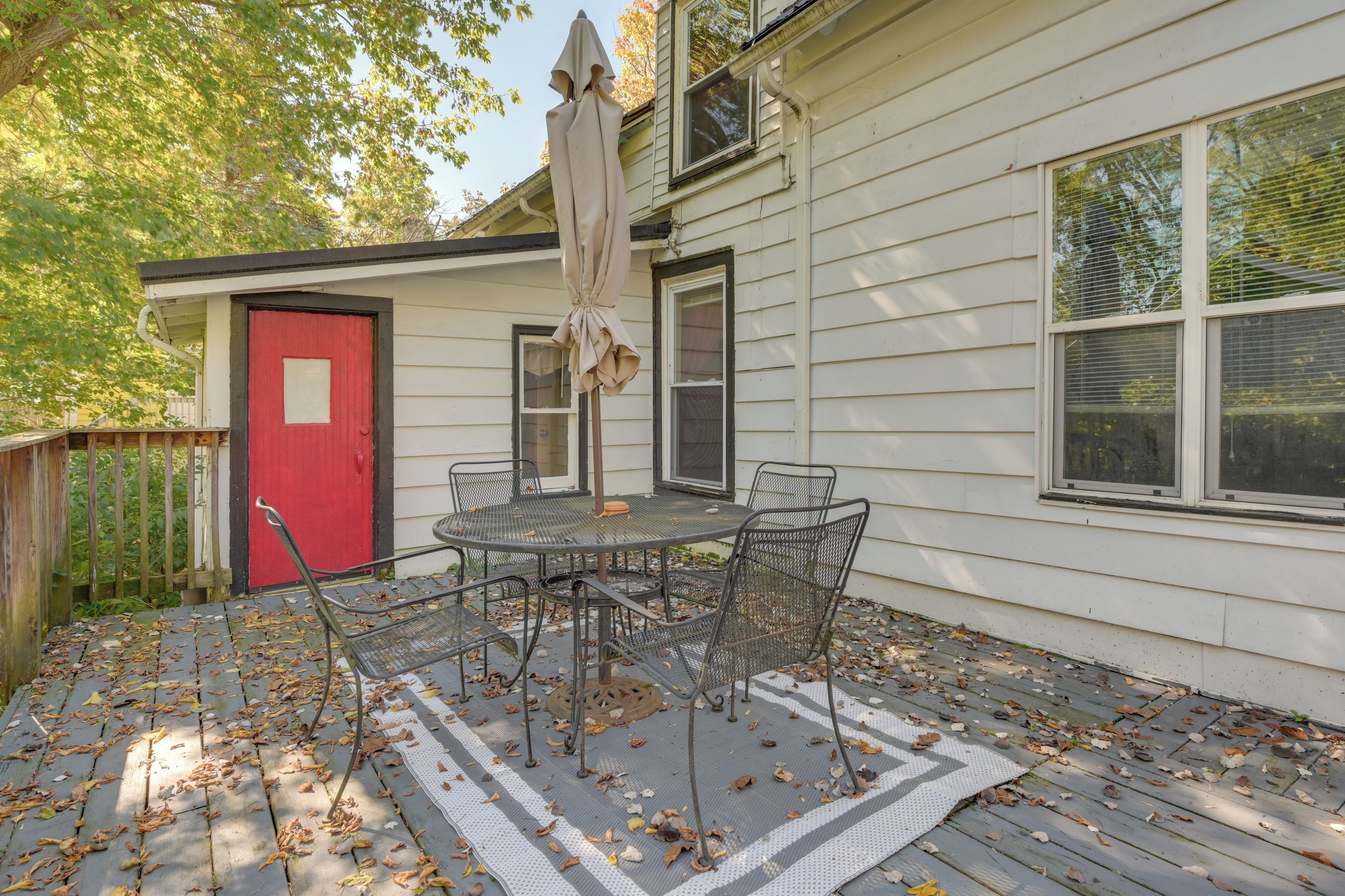 Une terrasse avec une table et des chaises, une porte rouge et un parasol.