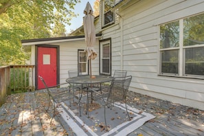 Une terrasse avec une table et des chaises, une porte rouge et un parasol.