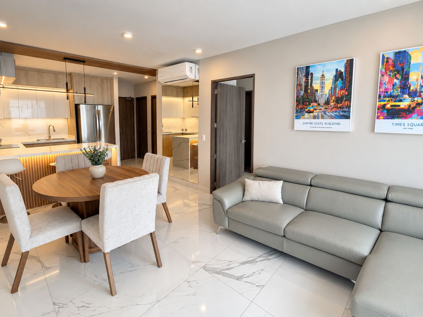 A modern living room with a dining area, a grey sofa, and a kitchen in the background.