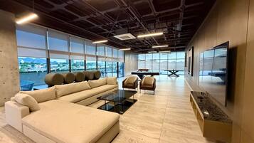 A modern lounge with a sofa, chairs, a pool table, and a large TV.