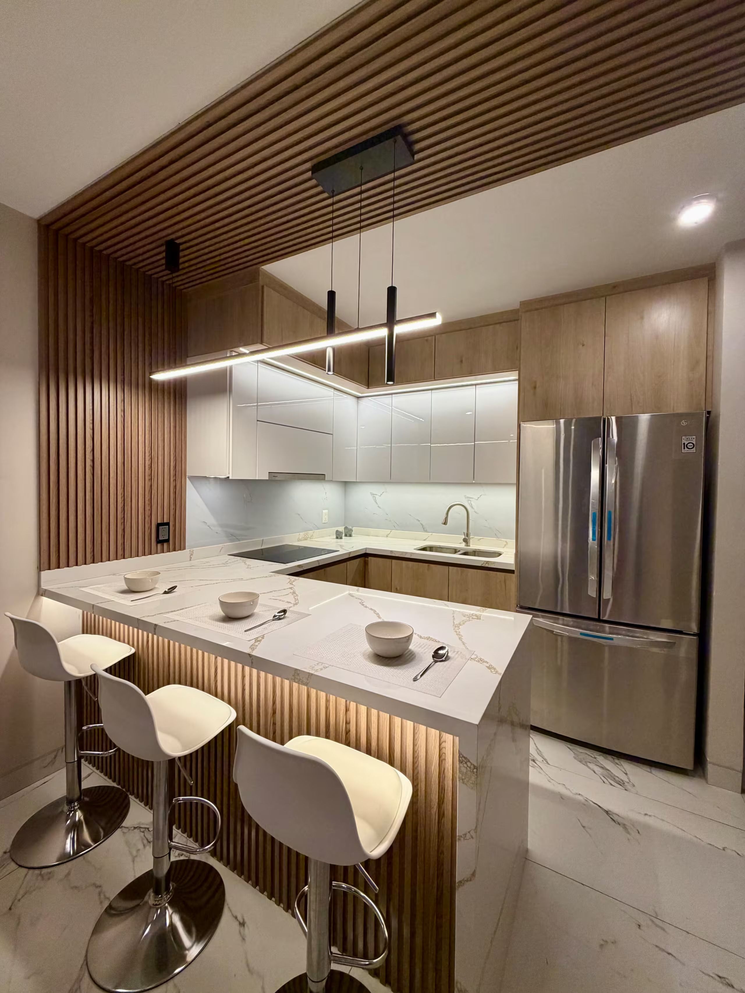 A modern kitchen with a central island, bar stools, stainless steel appliances, and wooden paneling.