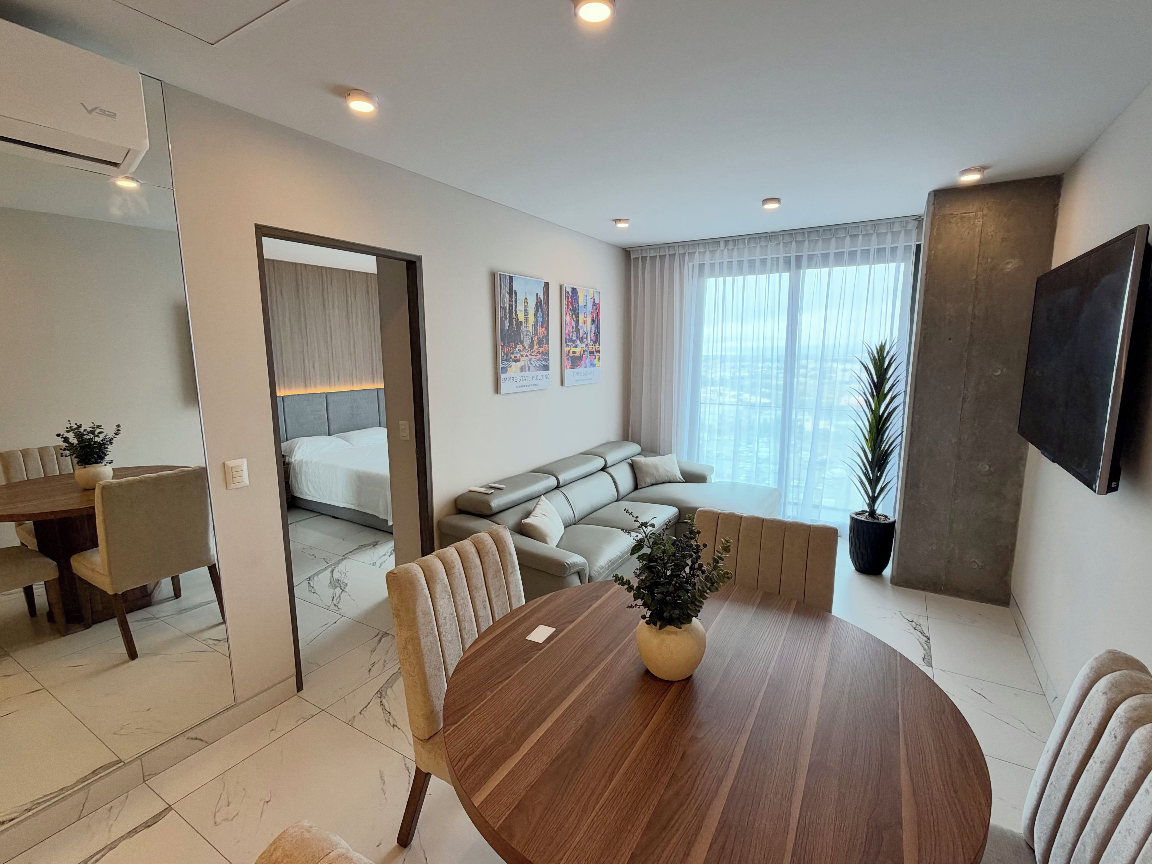 A modern living room with a dining area, a sofa, a TV, and a large window.