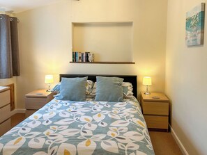 A neatly arranged bedroom with a bed, two bedside tables, a nightstand, a shelf with books, and a painting on the wall. - Ivy Cottage - UK51983 (Lancaster)