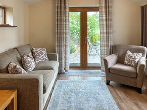 A living room with a sofa, armchair, and a view through a glass door to an outdoor area. - Ivy Cottage - UK51983 (Lancaster)