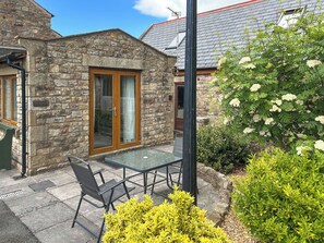 A stone cottage with a glass door, a patio table, and chairs. - Ivy Cottage - UK51983 (Lancaster)