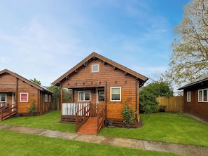 A wooden cabin with a porch and a small staircase leading to the entrance. - Log Cabin Two - UK51960 (Sutton-on-Sea)