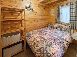 Een houten kamer met een bed, een plank en een raam met gordijnen.