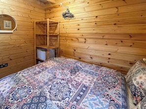 A wooden cabin room with a bed, a hanging chair, and a shelf unit. - Log Cabin Two - UK51960 (Sutton-on-Sea)