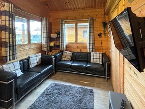 A cozy cabin interior with a black leather sofa set, a grey shag rug, and a flat-screen TV mounted on the wall. - Log Cabin Two - UK51960 (Sutton-on-Sea)