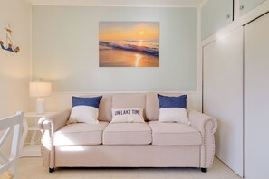 A beige sofa with 'ON LAKE TIME' pillow, a lamp, and a sunset painting on the wall. - Lakefront Escape at Sunrise Side Resort (Greenbush)