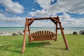 Un ensemble de balançoires en bois installé dans une zone herbeuse, avec vue sur l’océan et des rochers en arrière-plan.