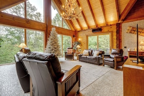 A log cabin interior with a fireplace, leather sofas, a Christmas tree, and large windows. - Game Room, Hot Tub! Retreat 3 Mi to Holiday Valley (Ellicottville)