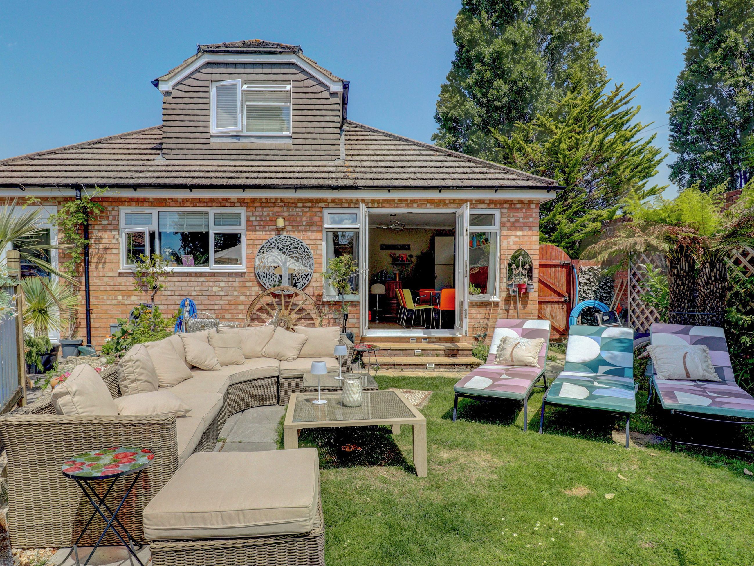 A house with a covered patio, outdoor seating, and a garden.