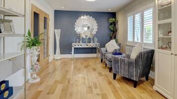 A room with a wooden parquet floor, a console table with decorative mirrors, striped armchairs, and a white cabinet with glass doors.
