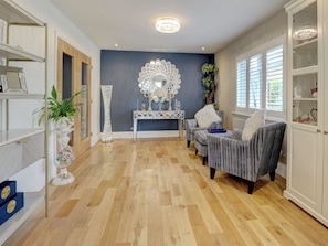 A room with a wooden parquet floor, a console table with decorative mirrors, striped armchairs, and a white cabinet with glass doors.