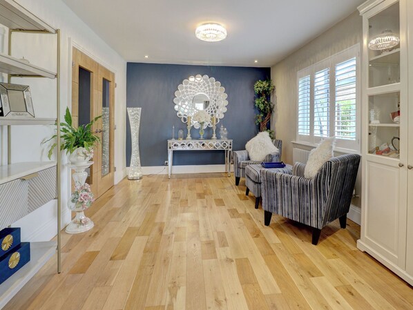 A room with a wooden parquet floor, a console table with decorative mirrors, striped armchairs, and a white cabinet with glass doors.