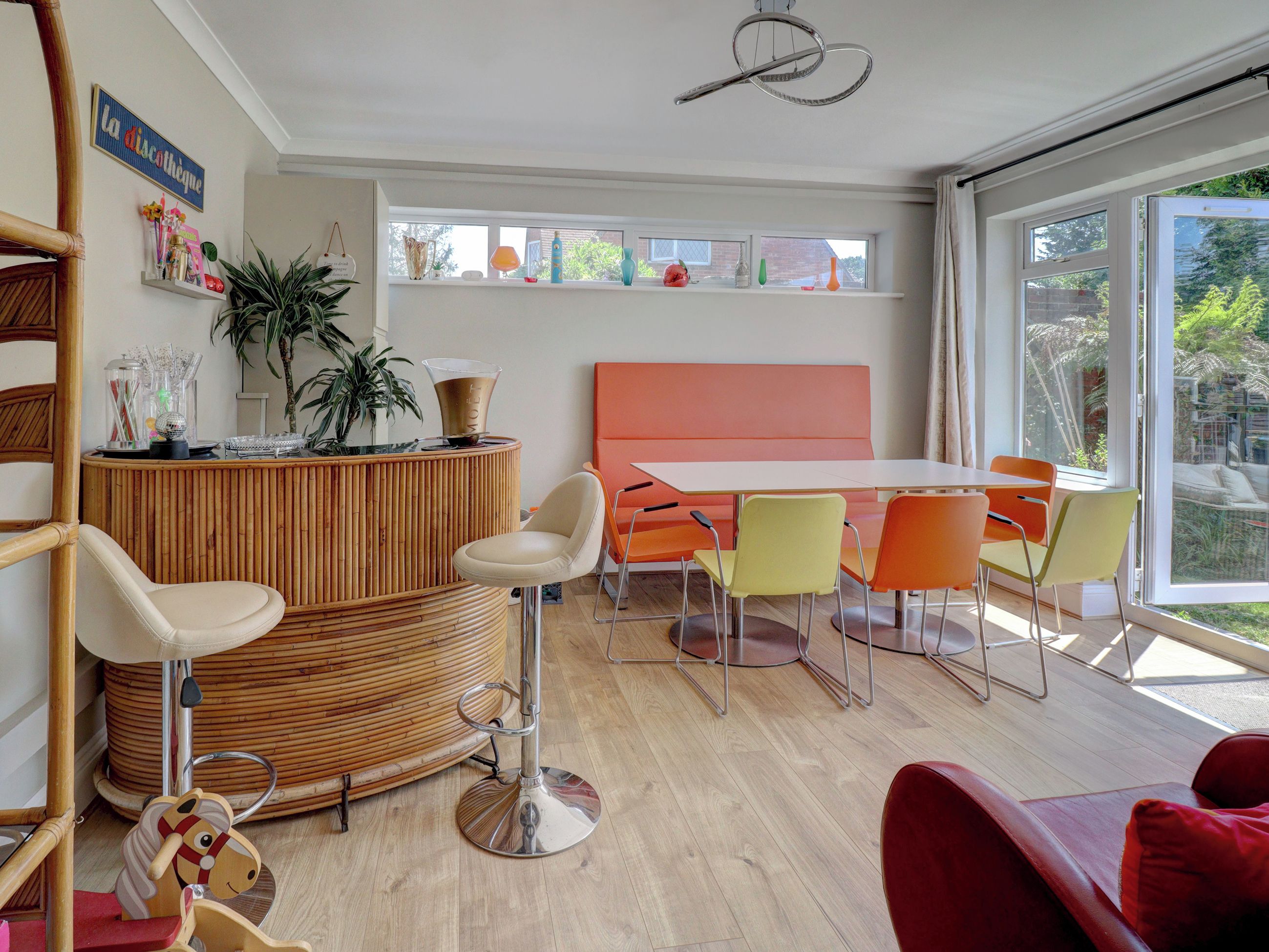 A modern interior with a round wooden reception desk, a white table with orange chairs, and a large window offering a view of greenery.