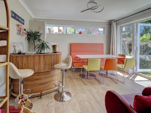 A modern interior with a round wooden reception desk, a white table with orange chairs, and a large window offering a view of greenery. - Boutique Gathering House (Park Gate)