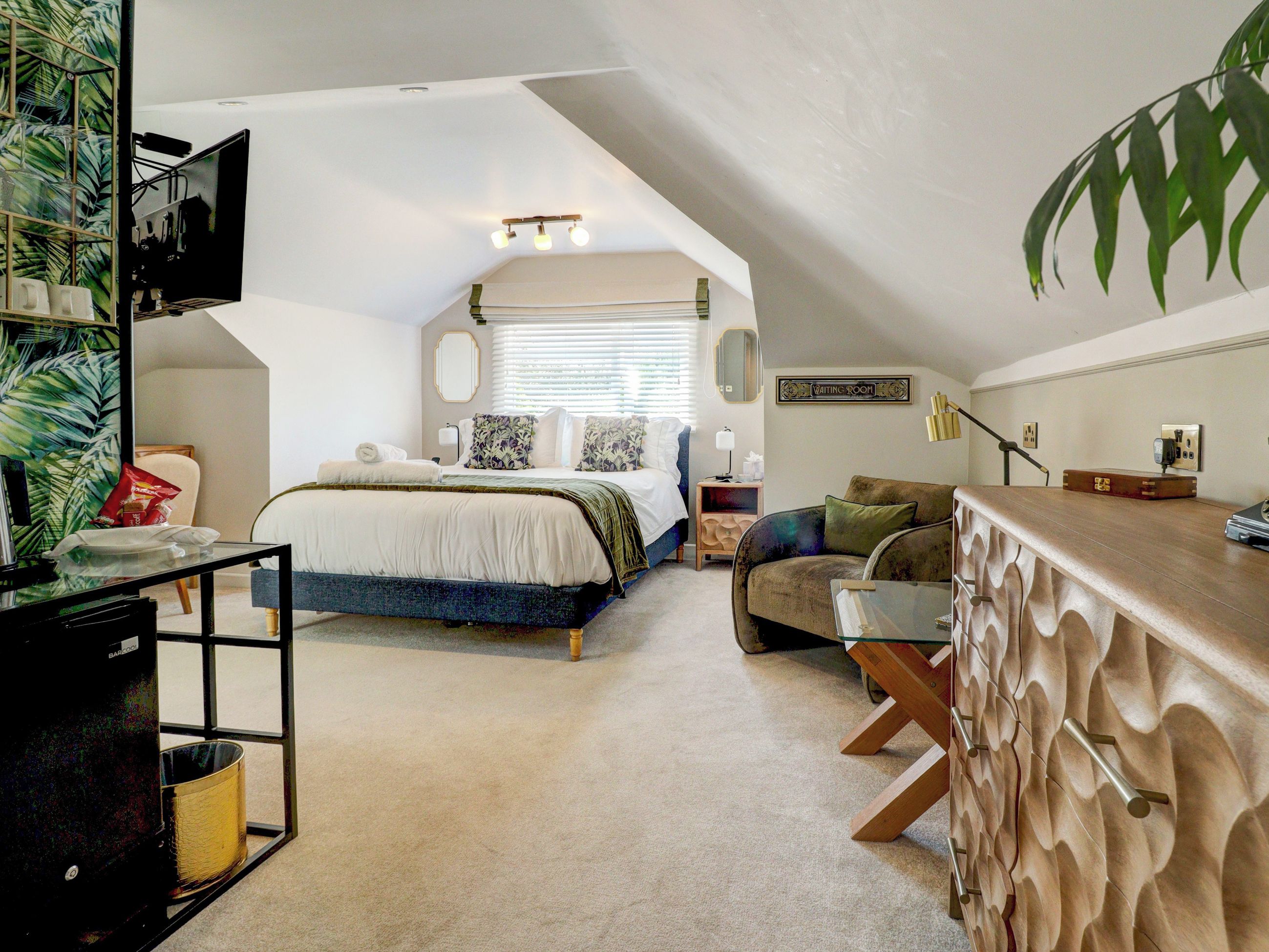 A bedroom with a bed, a sitting area with a sofa, a desk, and a large window with blinds.