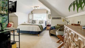 A bedroom with a bed, a sitting area with a sofa, a desk, and a large window with blinds.
