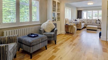 A spacious living room with striped upholstered furniture, a radiator, and large windows with shutters.