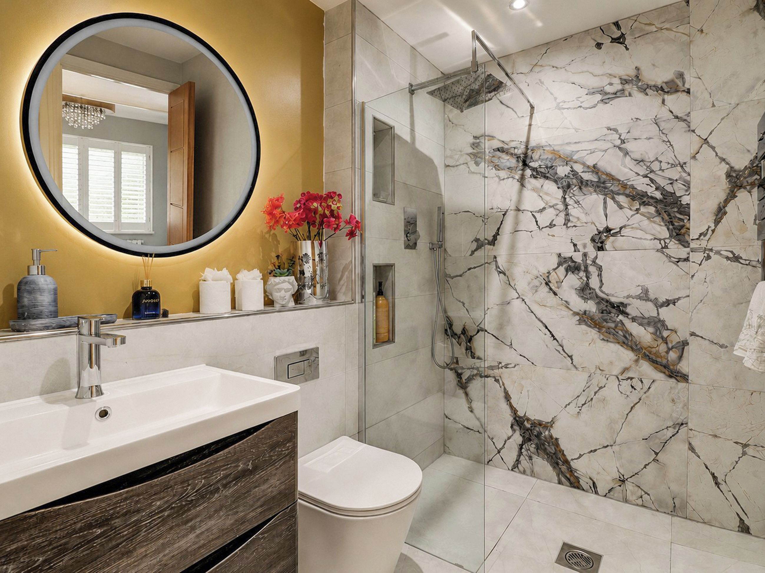 A modern bathroom with a marble shower, a round mirror, and a wooden vanity.
