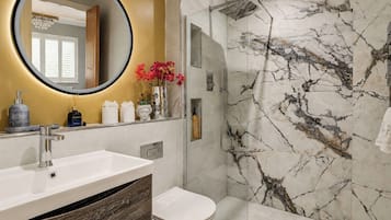 A modern bathroom with a marble shower, a round mirror, and a wooden vanity.