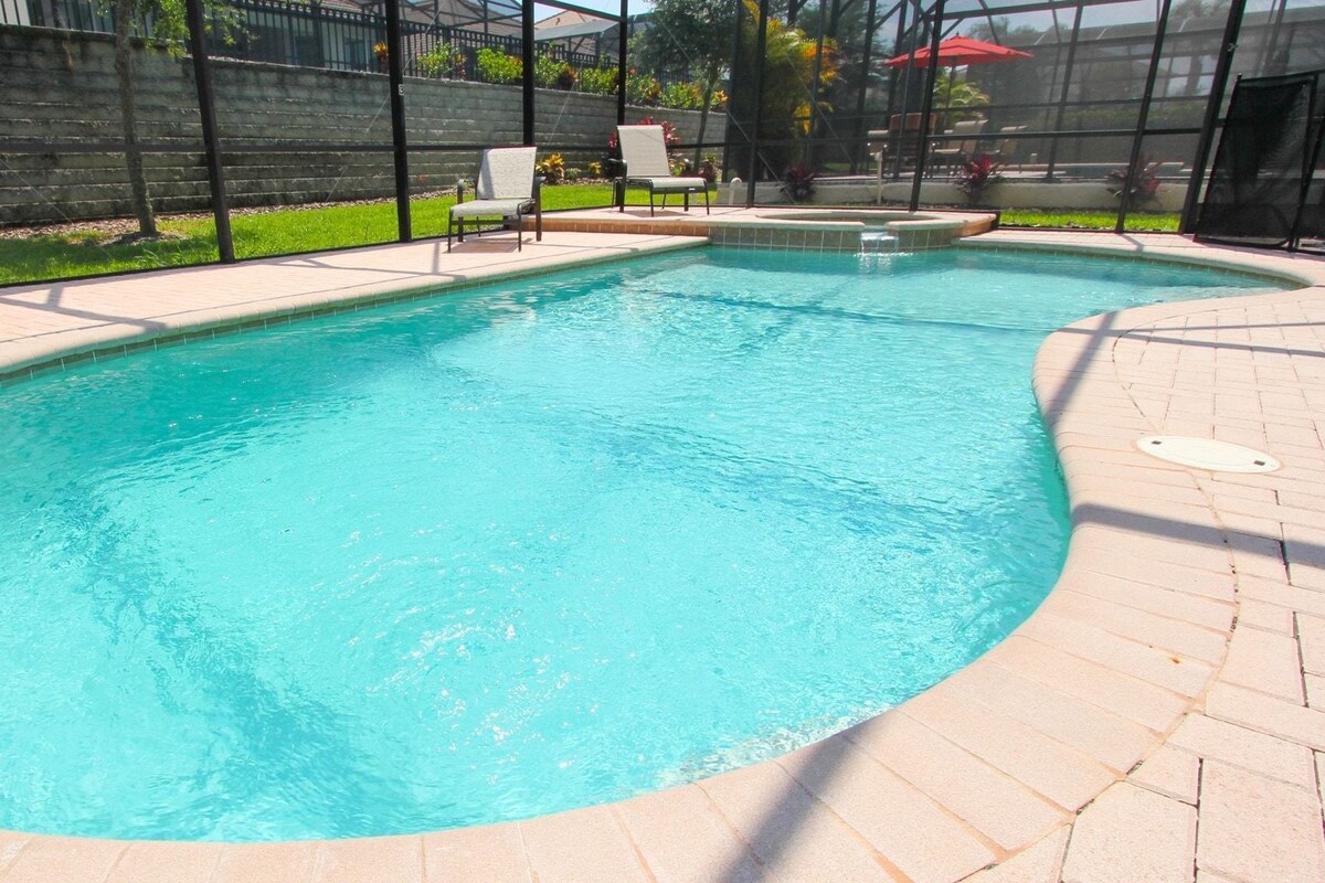 A swimming pool with a tiled deck, surrounded by a fence and chairs.