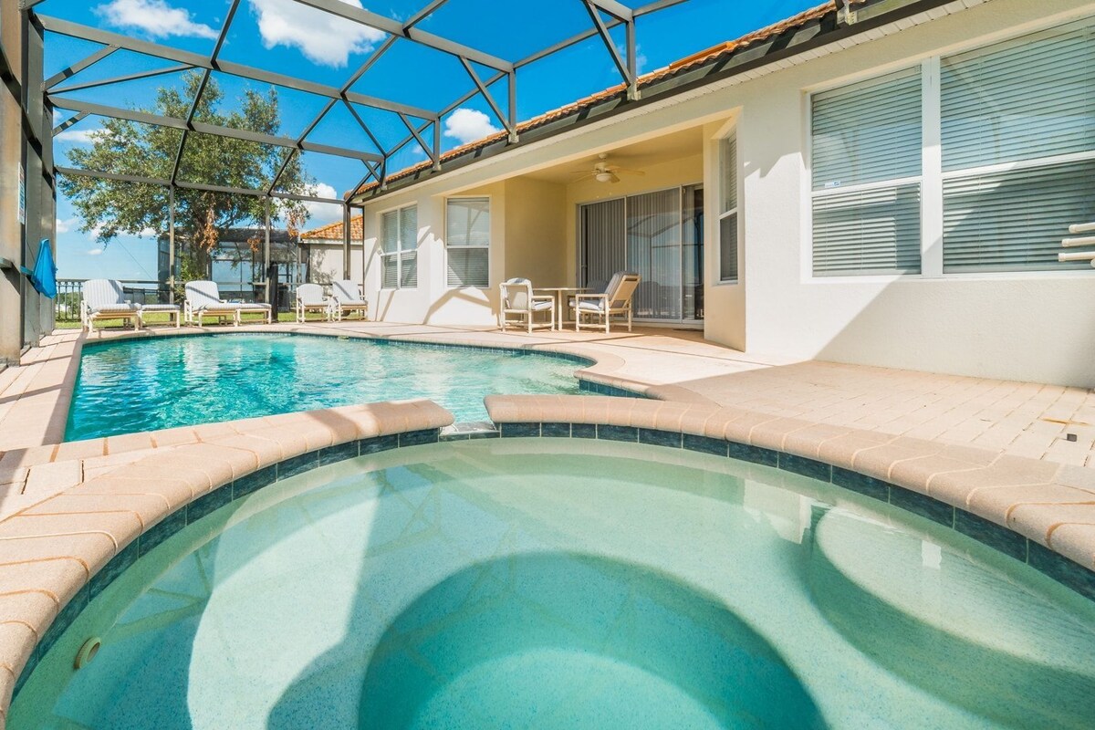 A swimming pool with a glass ceiling, surrounded by lounge chairs and a patio area.