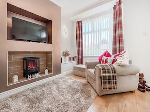 A living room with a fireplace, a sofa, a television, and a window with curtains. - 2 bedroom accommodation in Guisborough (Guisborough)