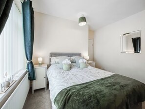 A bedroom with a bed, bedside tables, a nightstand, a window with curtains, a mirror, and a ceiling light. - 2 bedroom accommodation in Guisborough (Guisborough)