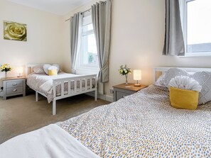 A bedroom with two beds, a nightstand with a lamp, a bedside table with a vase of flowers, and a window with curtains. - 2 bedroom accommodation in Guisborough (Guisborough)