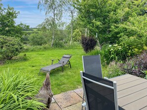 A garden with two lounge chairs and a table, surrounded by greenery and trees. - Verbena Cottage - UK52179 (Beaworthy)