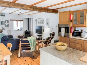 A cozy living room with a sofa, a television, and a fireplace. There is a dining area with a table and chairs. The kitchen has wooden cabinets and a microwave. - Verbena Cottage - UK52179 (Beaworthy)