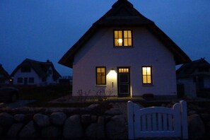 A two-story house with a gabled roof, a front porch with a bench, and a well-lit entrance. - Thatched house "Hygge Huus" (Zierow)