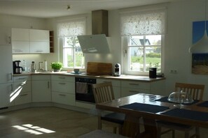 A kitchen with white cabinets, a wooden table, and a view of the outdoors through large windows. - Thatched house "Hygge Huus" (Zierow)