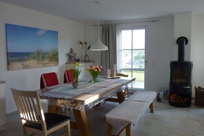 A dining area with a wooden table, chairs, a bench, a painting, a vase with flowers, and a wood-burning stove. - Thatched house "Hygge Huus" (Zierow)
